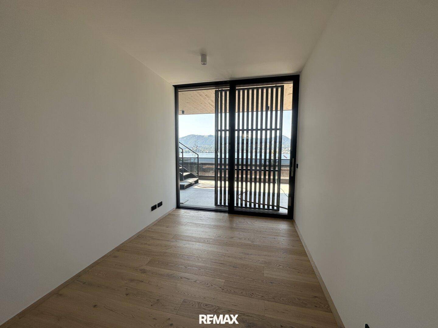 Schlichtes Zimmer mit Holzboden und Zugang zu einer Außenterrasse mit Seeblick.