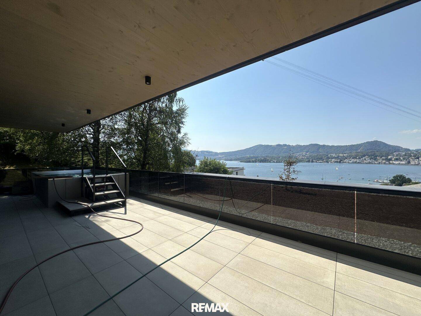 Weitläufige Terrasse mit Fliesenboden, einem Whirlpool und Panoramablick auf den See und die Berge.