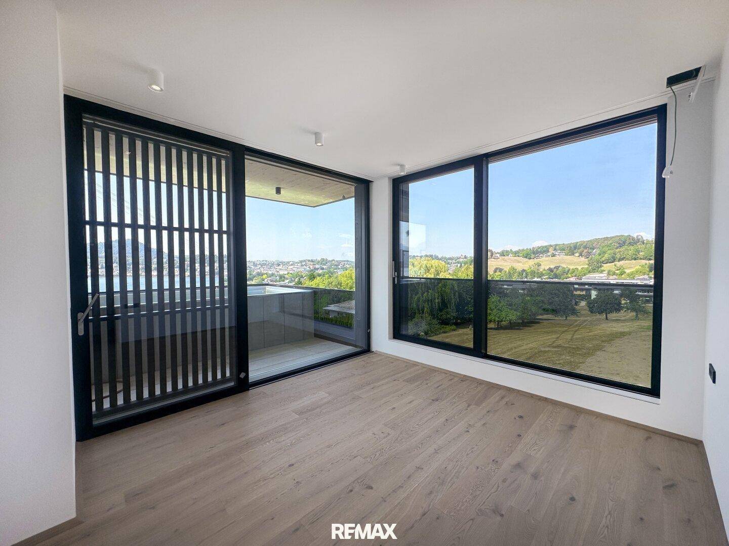 Lichtdurchfluteter Raum mit Holzboden, bodentiefen Fenstern und Zugang zu einem Balkon mit Weitblick.