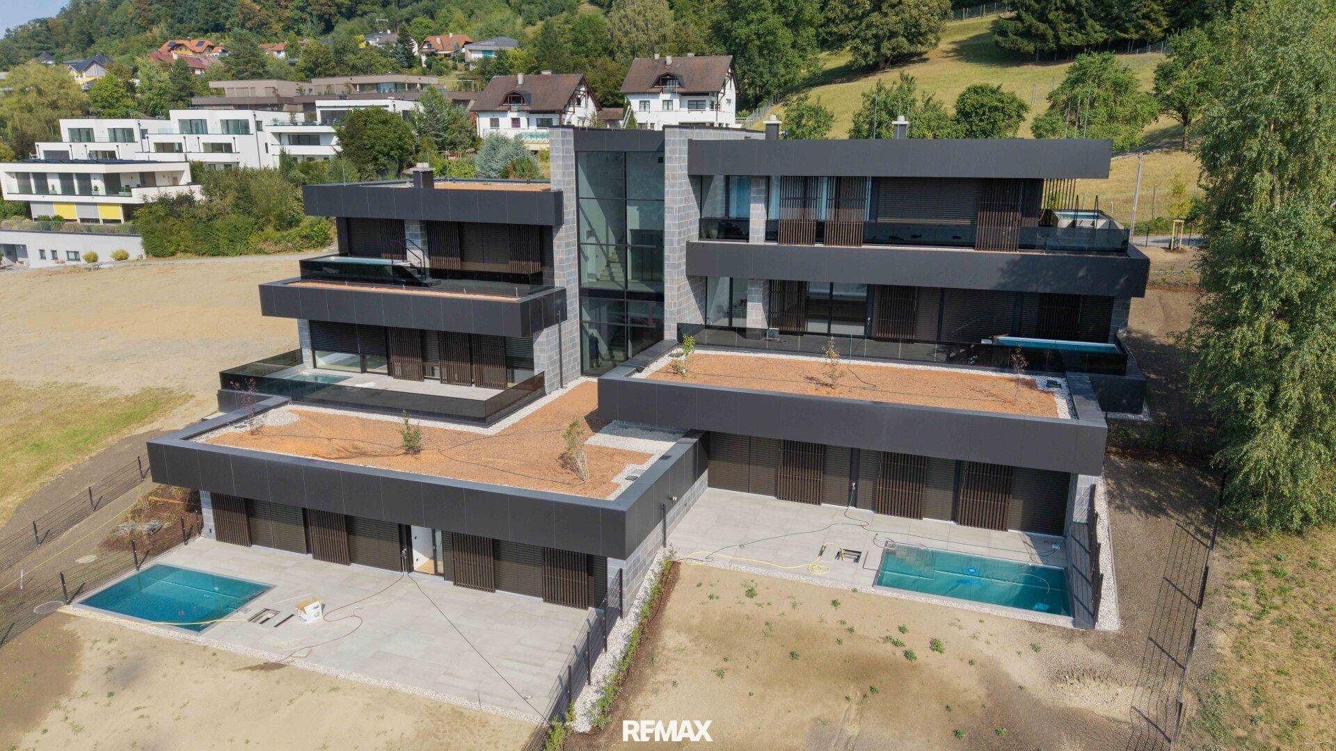 Moderne Villa mit dunkler Fassade, großen Glasflächen und mehreren Terrassen mit Pools in Hanglage.