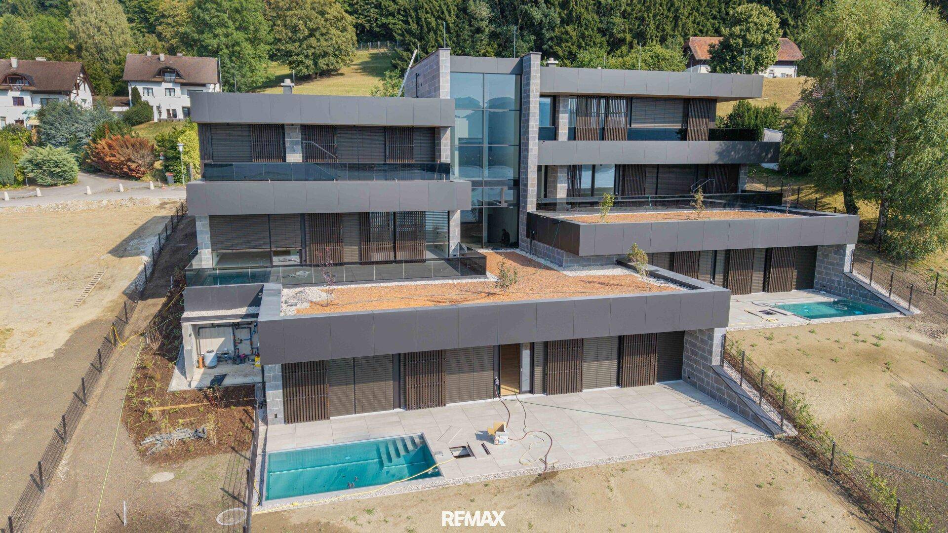 Moderne Architektur des Neubaus mit mehreren Ebenen, Balkonen und integrierten Pools in der Landschaft.