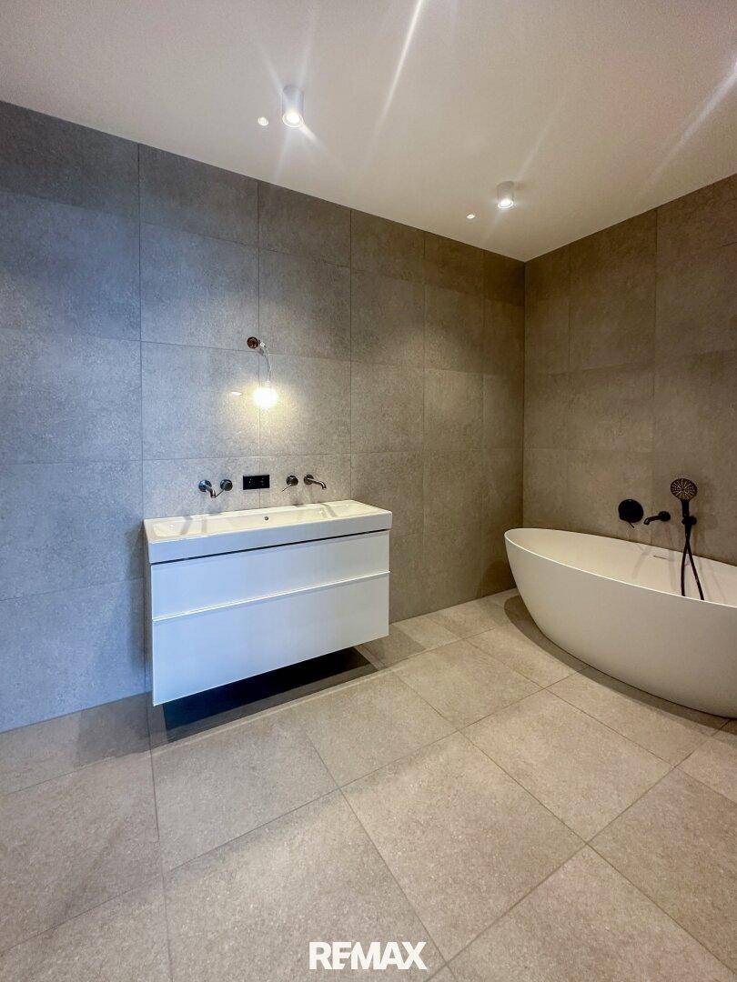 Modernes Badezimmer mit freistehender Badewanne, schwebendem Waschtisch und großformatigen Fliesen.