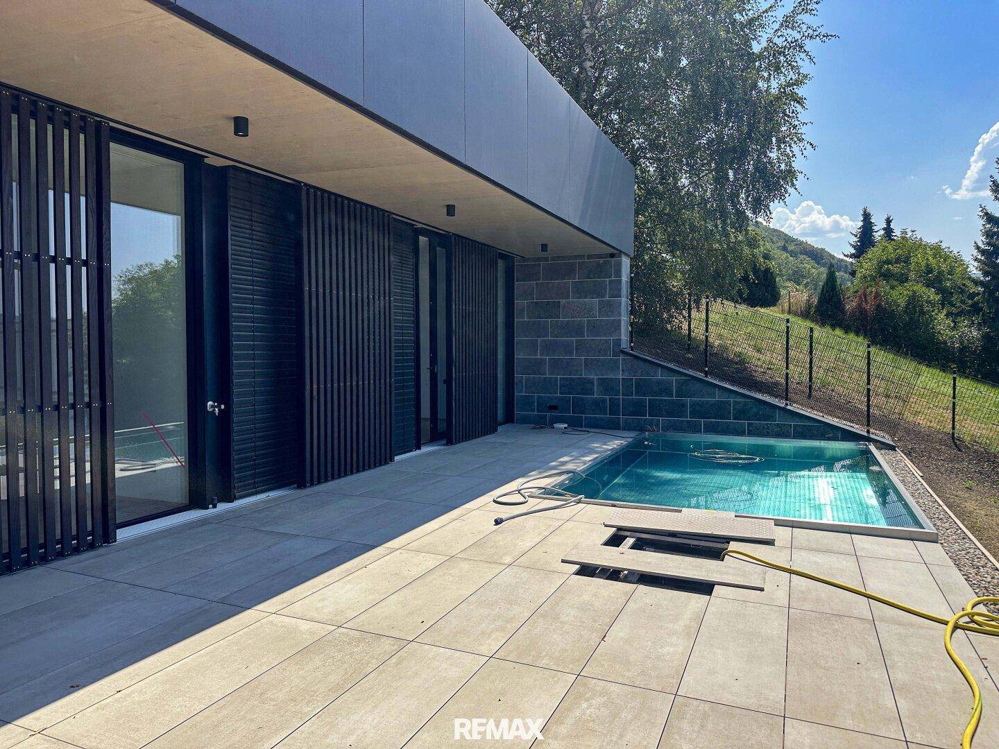 Moderne Architektur mit großzügiger Terrasse und integriertem Pool, umgeben von grüner Landschaft.