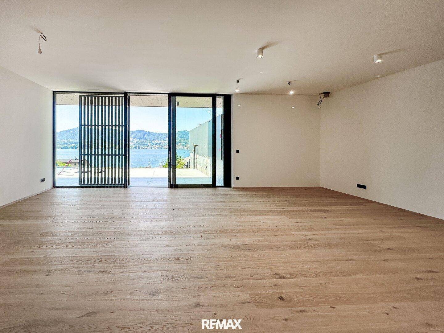 Heller, leerer Wohnraum mit Holzboden und großen Schiebetüren, die einen weiten Seeblick bieten.