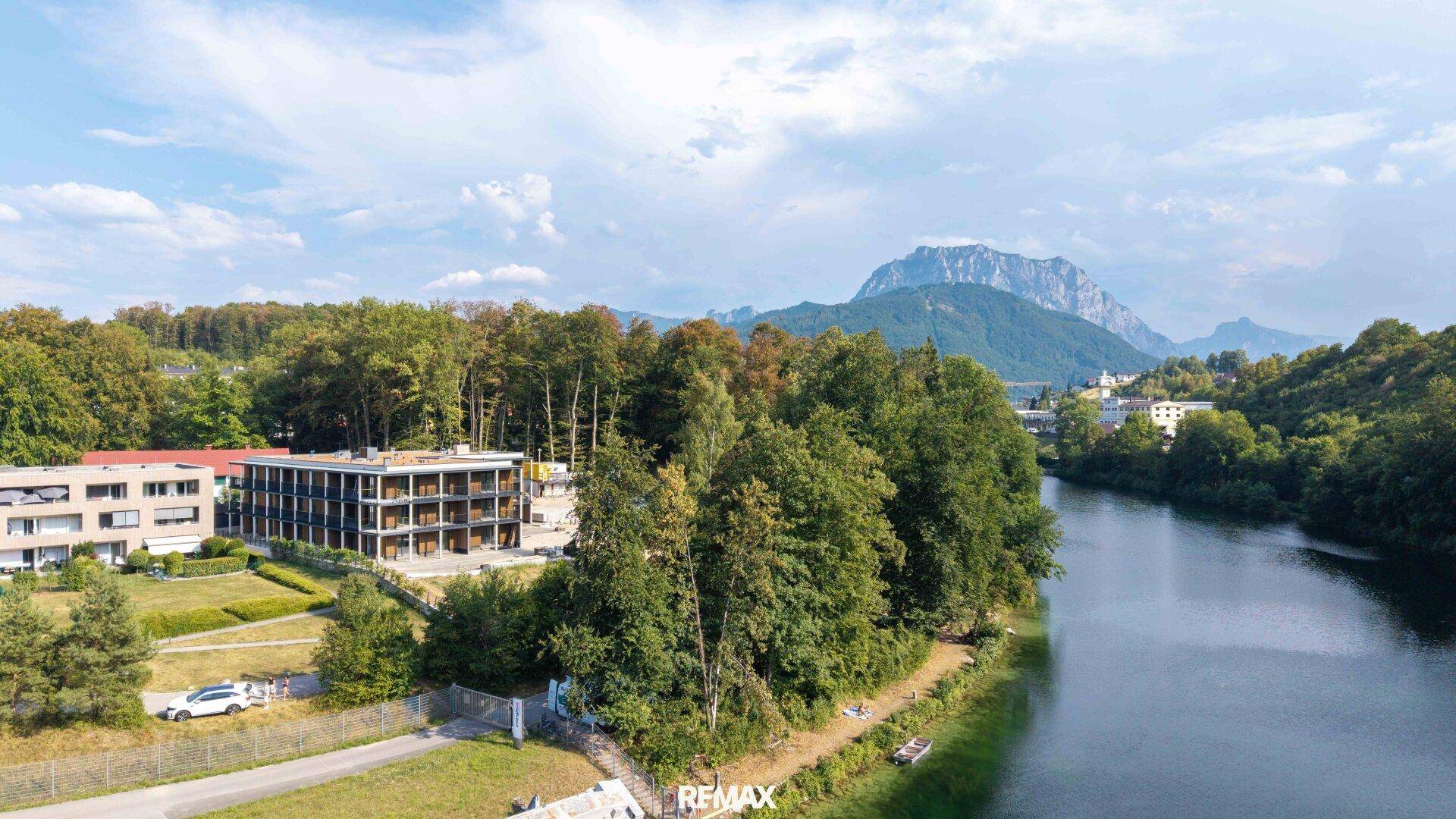 Weitläufige Luftaufnahme eines Neubaus am Flussufer mit Bergblick und umgebender Natur.