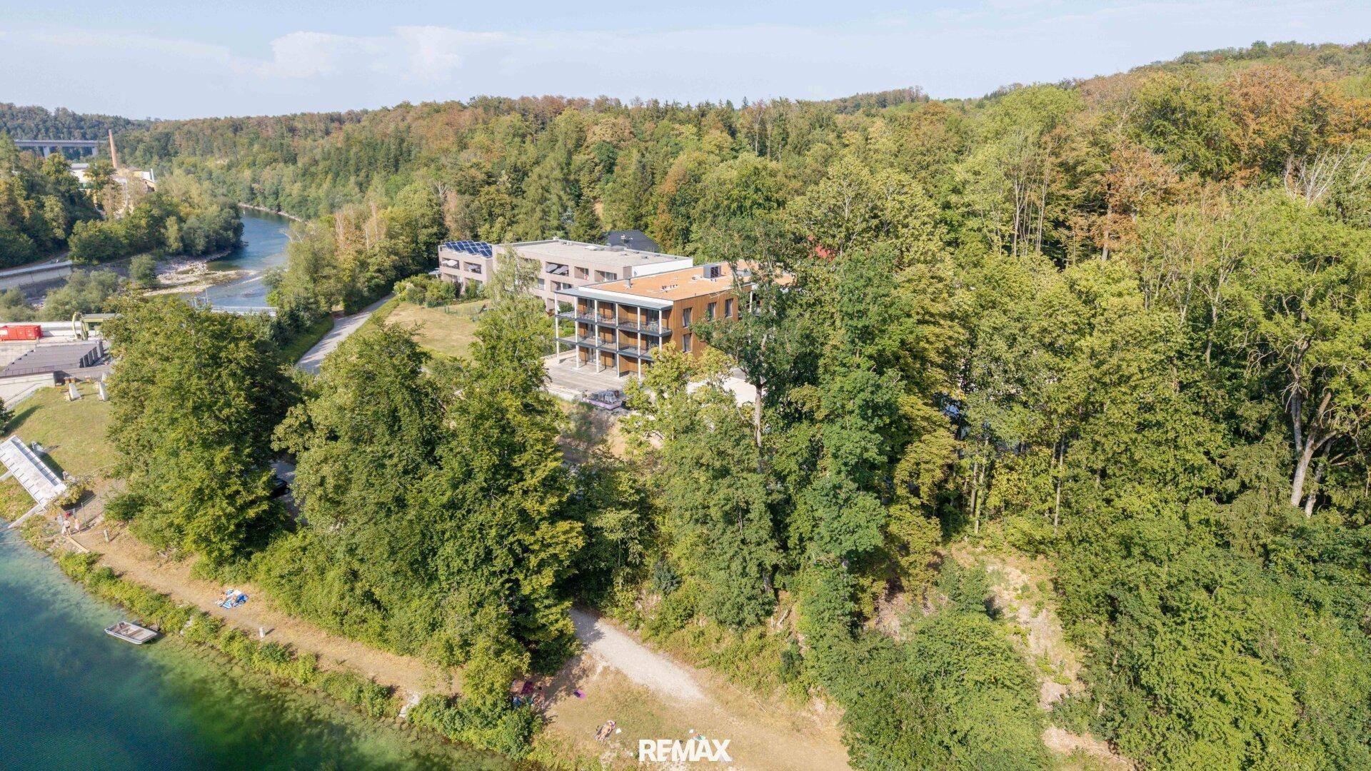 Panoramablick auf ein modernes Wohnhaus eingebettet in eine grüne Landschaft am Fluss mit Waldgebiet.