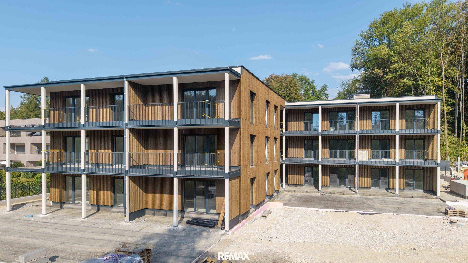 Moderne Fassade eines Neubaus mit Holzverkleidung und großzügigen Balkonen.