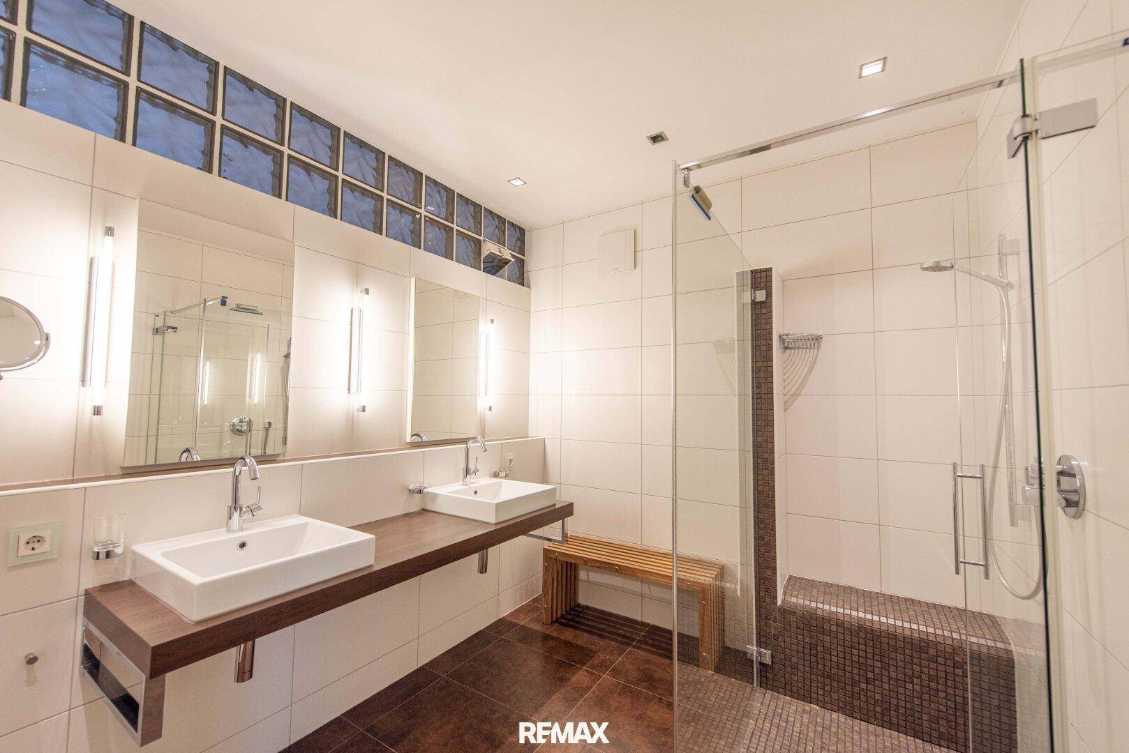 Modernes Badezimmer mit Doppelwaschbecken, großer begehbarer Dusche und Glasbaustein-Fensterband.