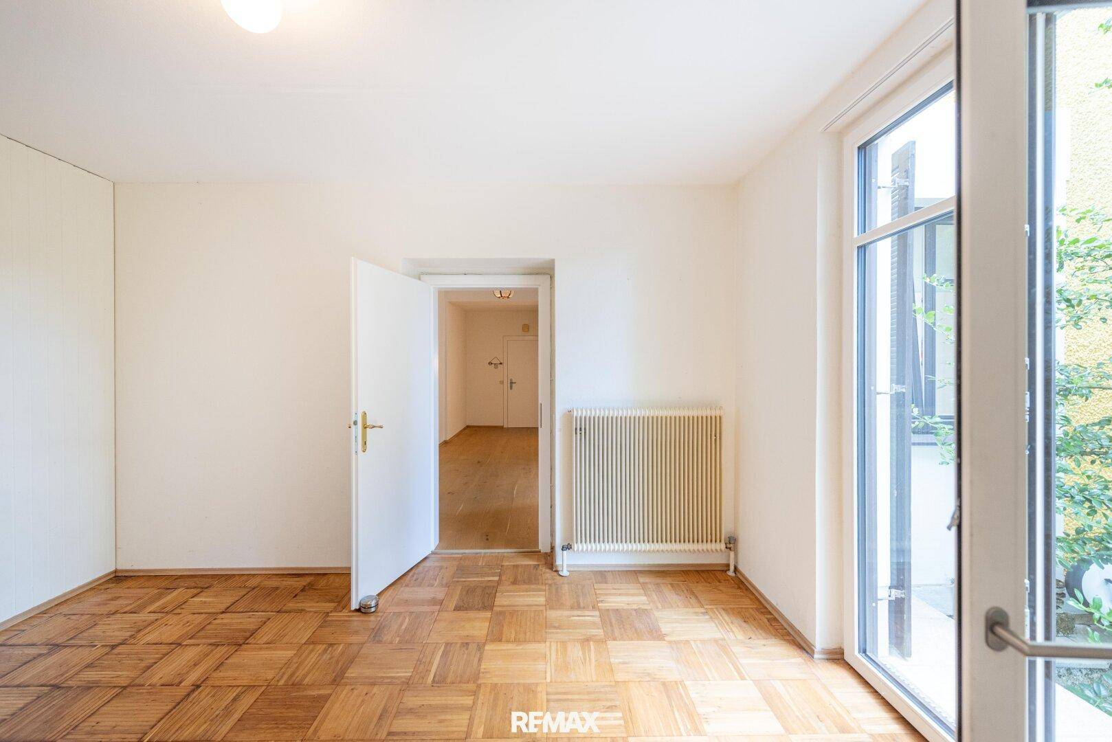 Freundliches Zimmer mit Parkettboden und großem Fenster, das viel Tageslicht hereinlässt.