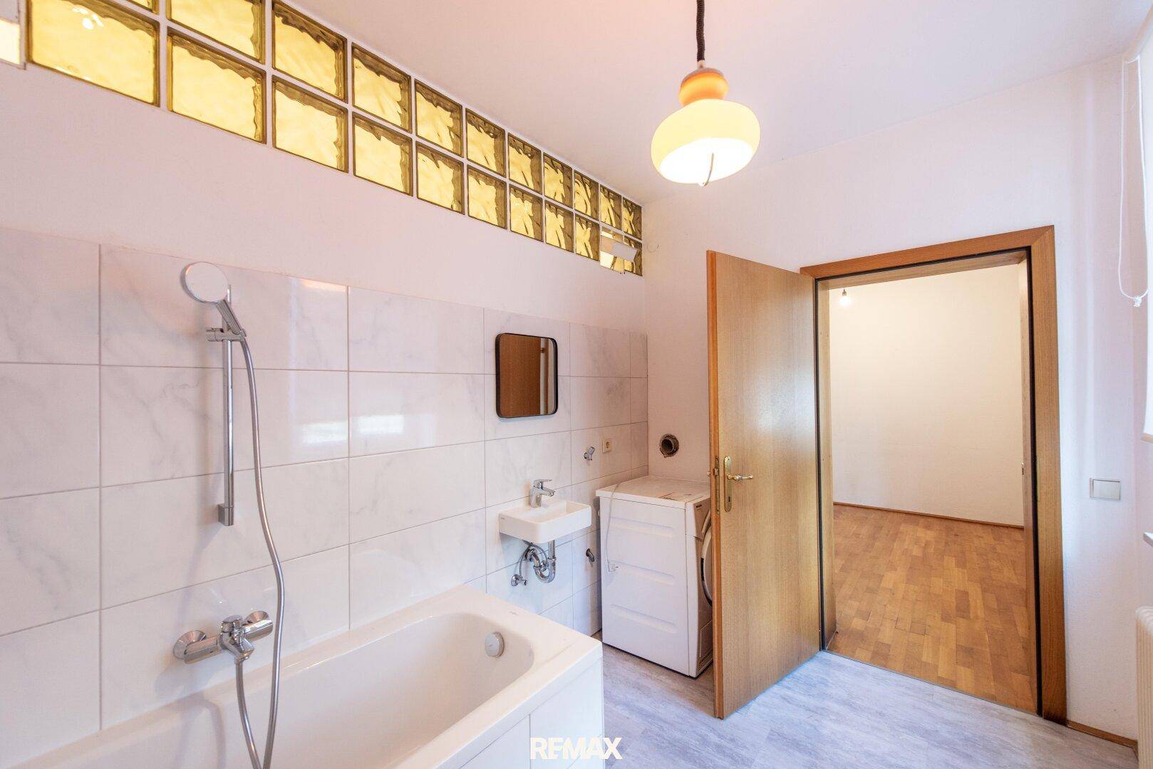 Badezimmer mit Badewanne, kleinem Waschbecken und Platz für eine Waschmaschine.