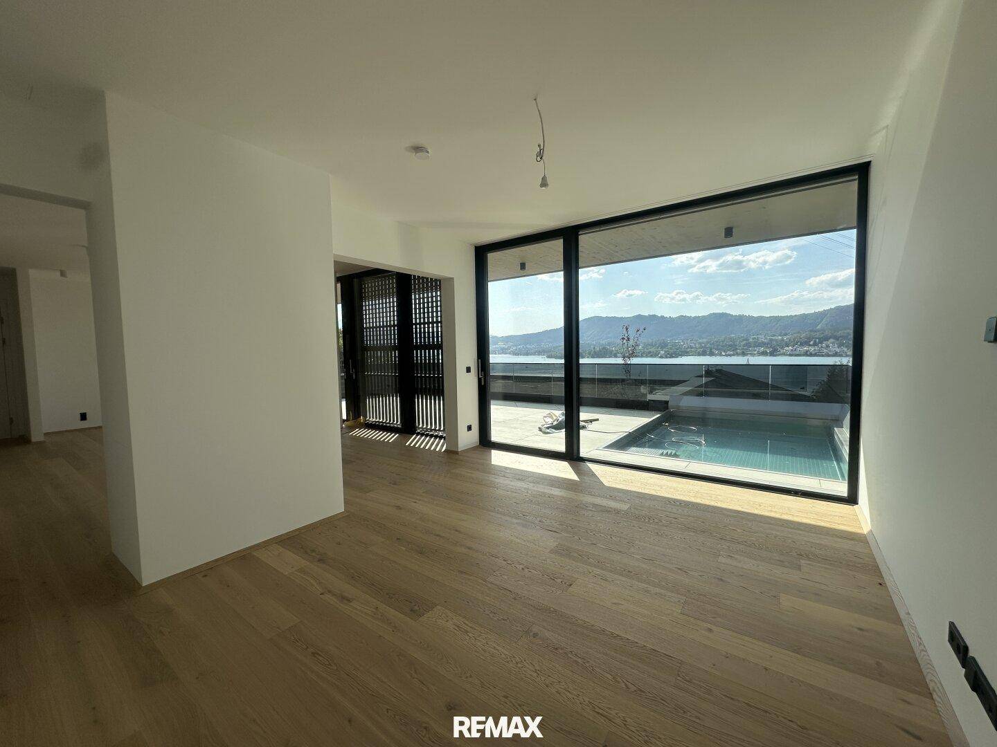 Heller Wohnbereich mit Eichenparkett, großen Fenstern und direktem Zugang zu einer Terrasse mit Pool und Seeblick.
