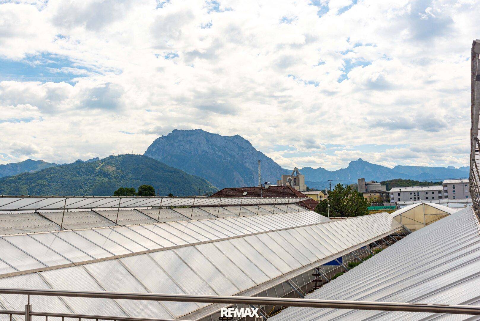 Weitblick auf die umliegende Berglandschaft über den Dächern der Gewächshäuser.