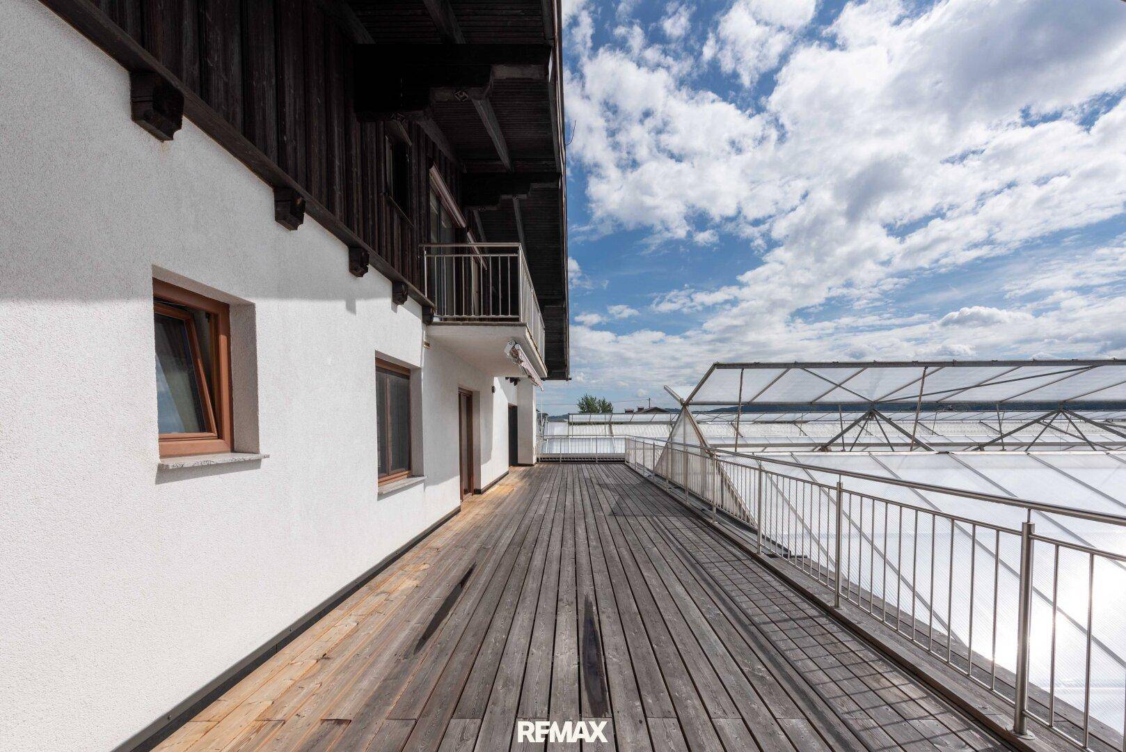 Geräumige Holzterrasse entlang der Hausfassade mit Blick auf die Umgebung.