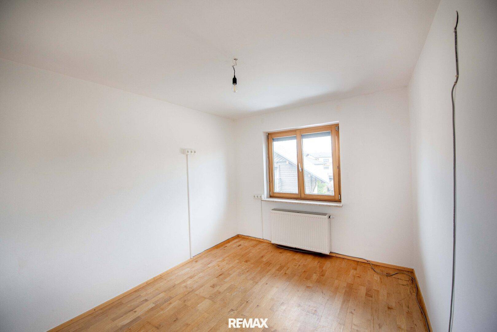 Helles Schlafzimmer mit Holzboden, weiß gestrichenen Wänden und einem Fenster.