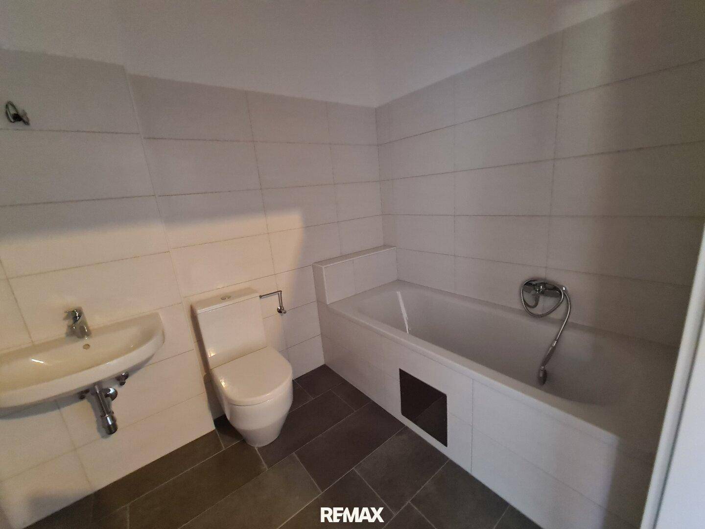 Modernes Badezimmer mit Badewanne, WC und Waschbecken, gefliest in Weiß und Grau.