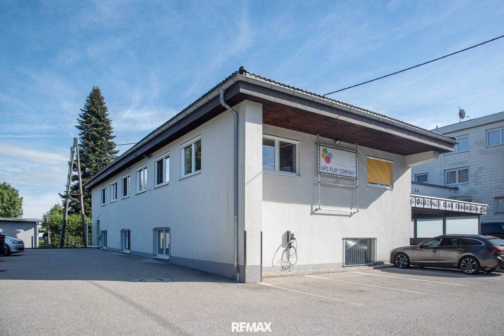 Seitenansicht des Gebäudes mit Parkplätzen und einer Ladestation für Elektrofahrzeuge an der Wand.