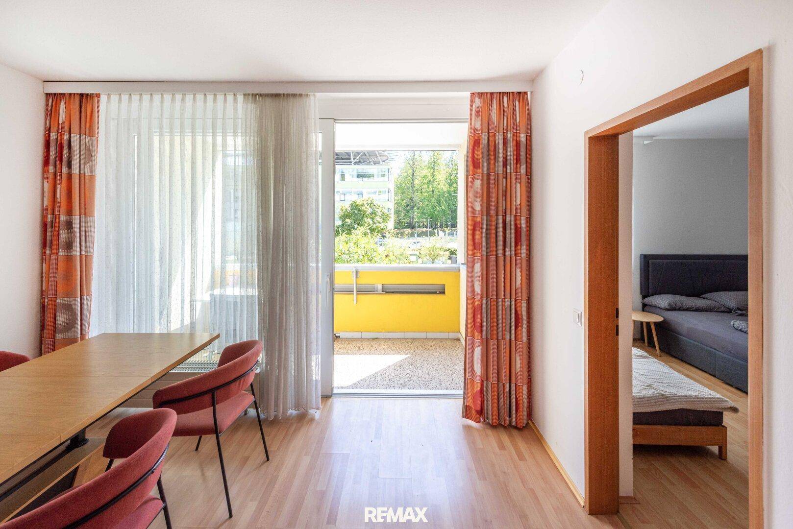 Essbereich mit Holztisch und Stühlen, direktem Zugang zum Balkon und Blick ins Schlafzimmer.