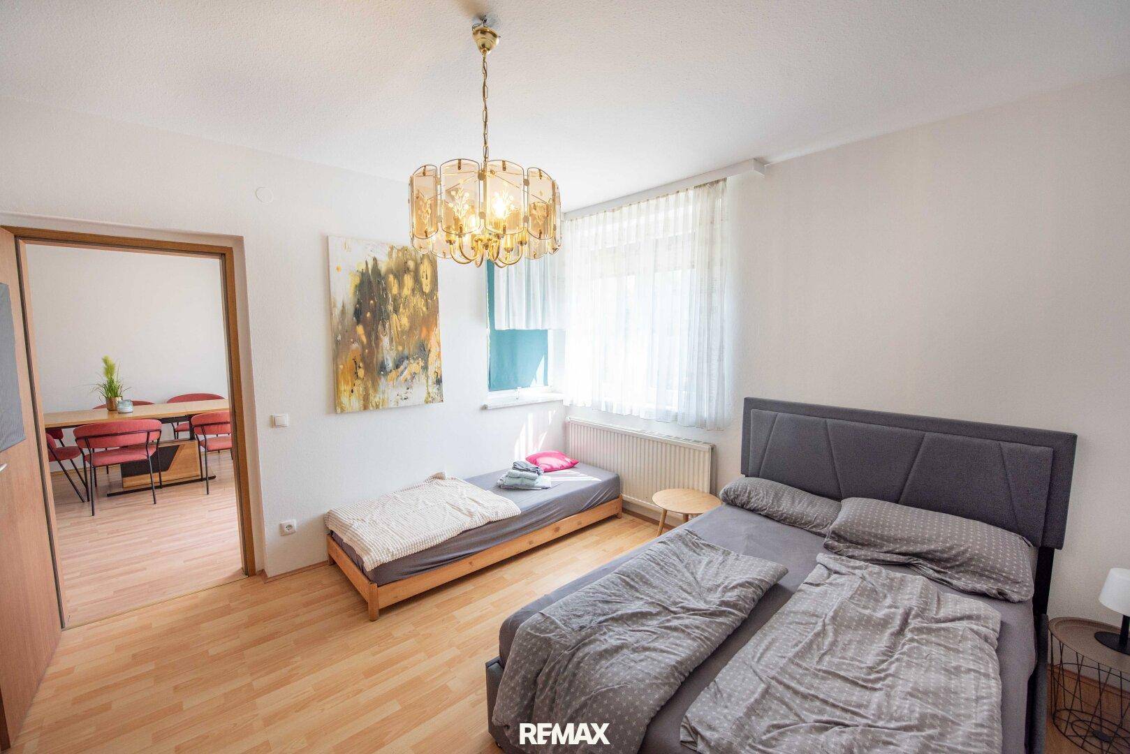 Helles Schlafzimmer mit zwei Betten, Holzfußboden und Zugang zum Wohnbereich.