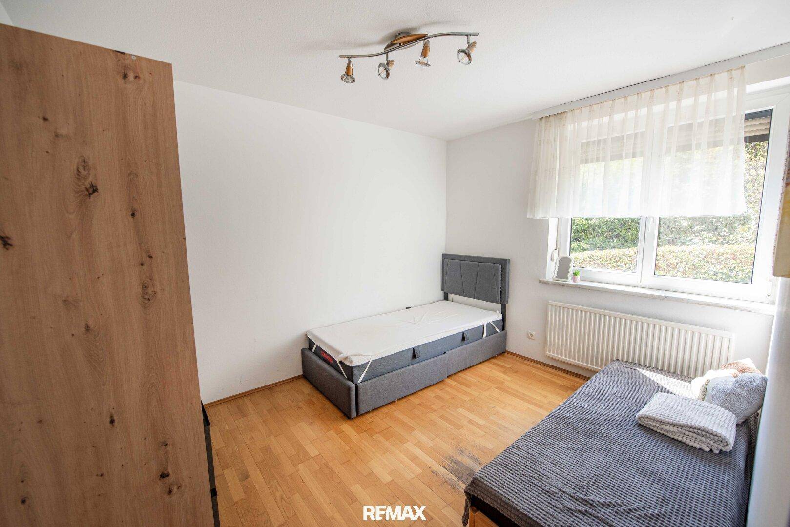 Schlafzimmer mit Einzelbett, Holzfußboden und Fenster mit Blick ins Grüne.