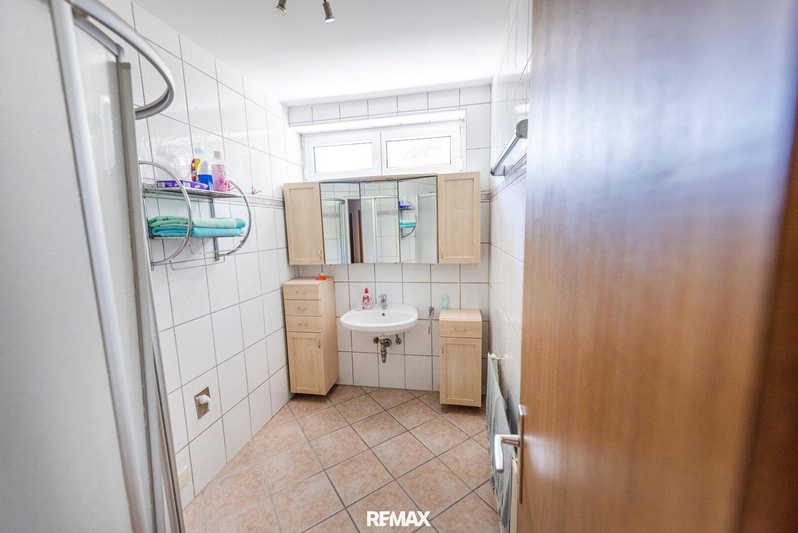Gefliestes Badezimmer mit Dusche, Waschbecken und Spiegelschrank.