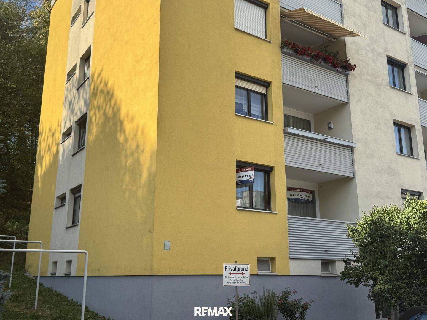 Nahaufnahme der gelben Fassade eines Wohngebäudes mit Balkonen und Fenstern.