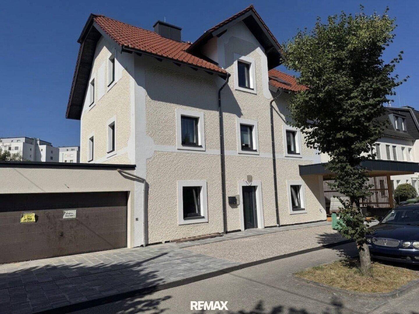 Vorderansicht eines Mehrfamilienhauses mit beiger Fassade, rotem Ziegeldach und integrierter Garage.