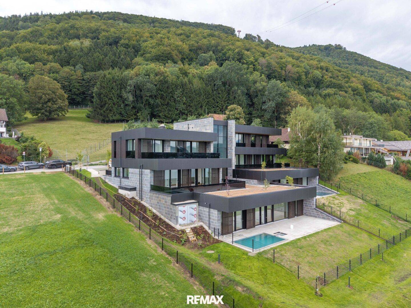 Beeindruckende moderne Villa am Hang mit mehreren Terrassen und Pools, umgeben von Wald und Natur.