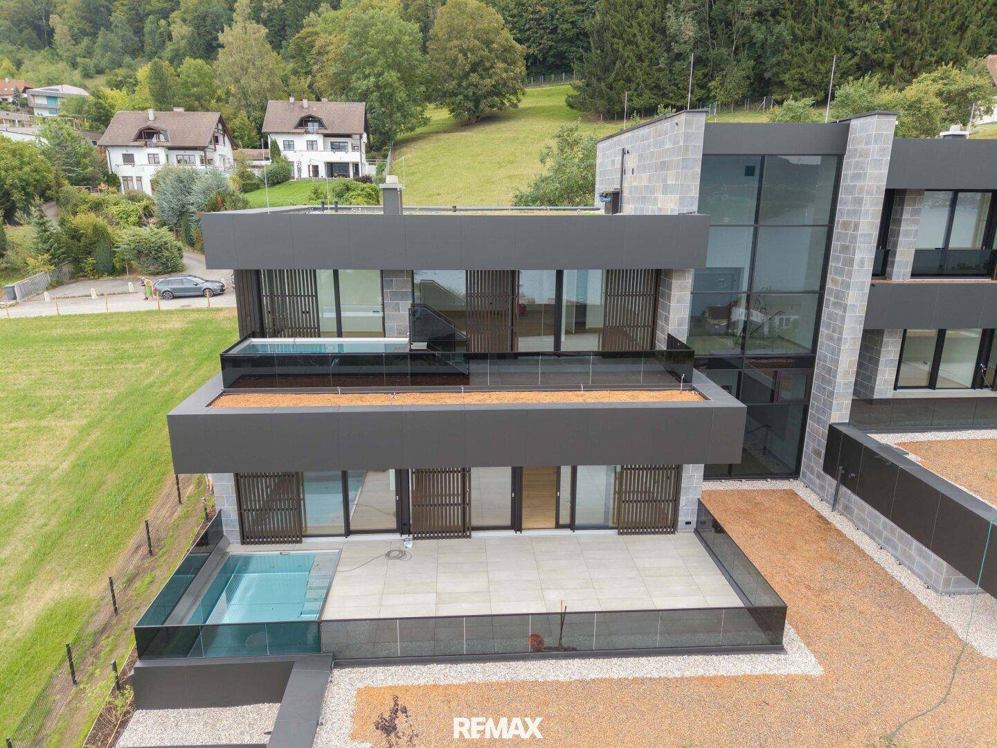Moderne Architektur mit mehreren Ebenen, Terrassen und integrierten Pools, umgeben von grüner Natur.