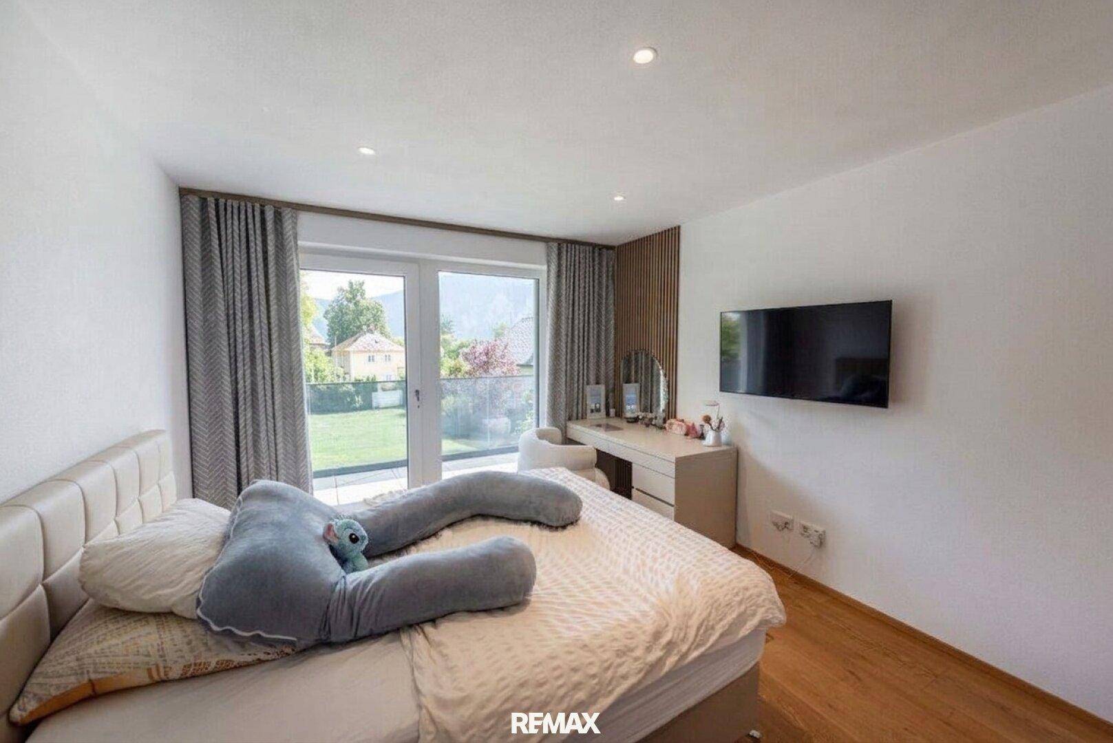 Helles Schlafzimmer mit Holzboden, Zugang zum Balkon und moderner Einrichtung.