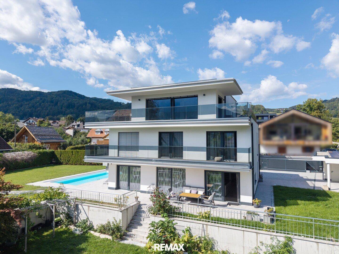 Elegante Villa mit Pool und weitläufigem Garten, umgeben von grüner Landschaft und Bergen.