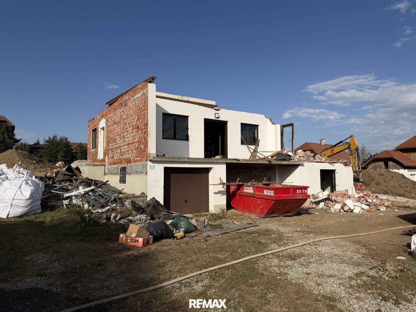 Haus im Umbau mit sichtbaren Ziegelwänden und Bauschutt, ein Bagger ist im Hintergrund zu sehen.