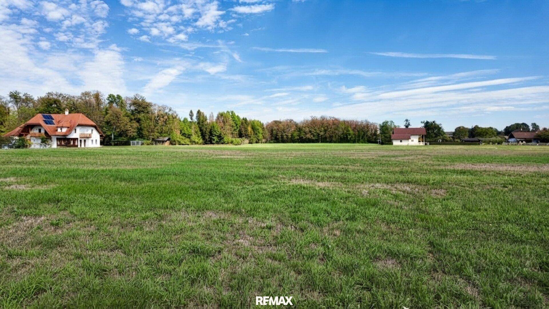 Idyllisches, offenes Grundstück mit weitem Blick über grüne Wiesen und charmante Häuser am Waldrand.