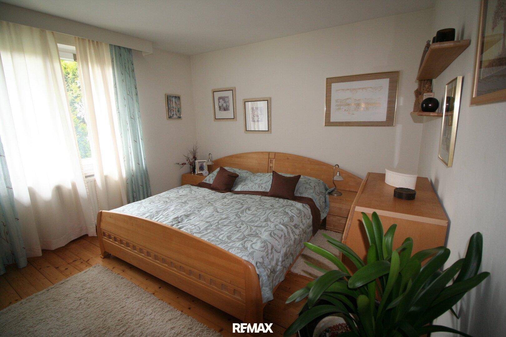 Helles Schlafzimmer mit einem Holzbett, passenden Nachttischen und einem großen Fenster mit Vorhängen.