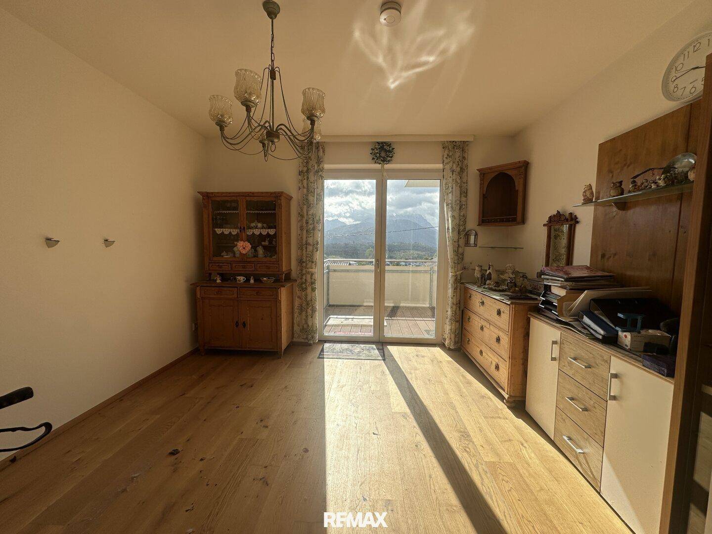 Gemütlicher Wohnbereich mit traditionellen Holzmöbeln, Parkettboden und Zugang zu einem Balkon mit Bergblick.
