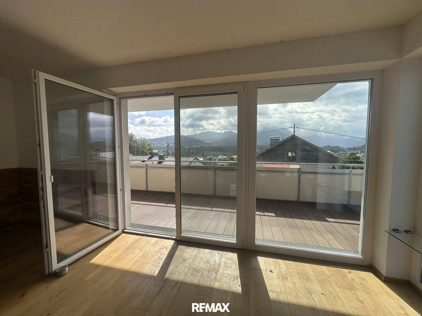 Heller Innenraum mit großen Schiebetüren, Holzboden und Zugang zu einer Terrasse mit Bergblick.