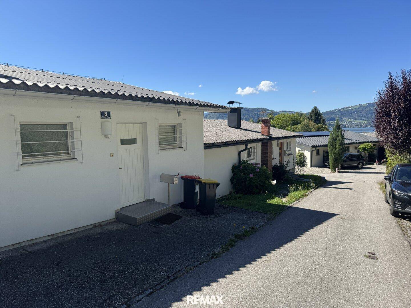 Ruhige Wohnstraße mit weißen Einfamilienhäusern und Blick auf die entfernte Seenlandschaft.