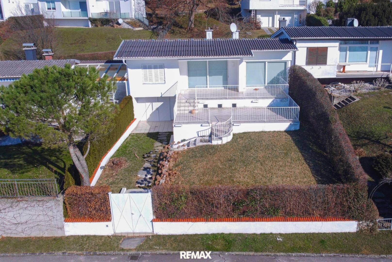 Luftaufnahme eines Einfamilienhauses mit Garten, Terrasse und umliegender Hecke.