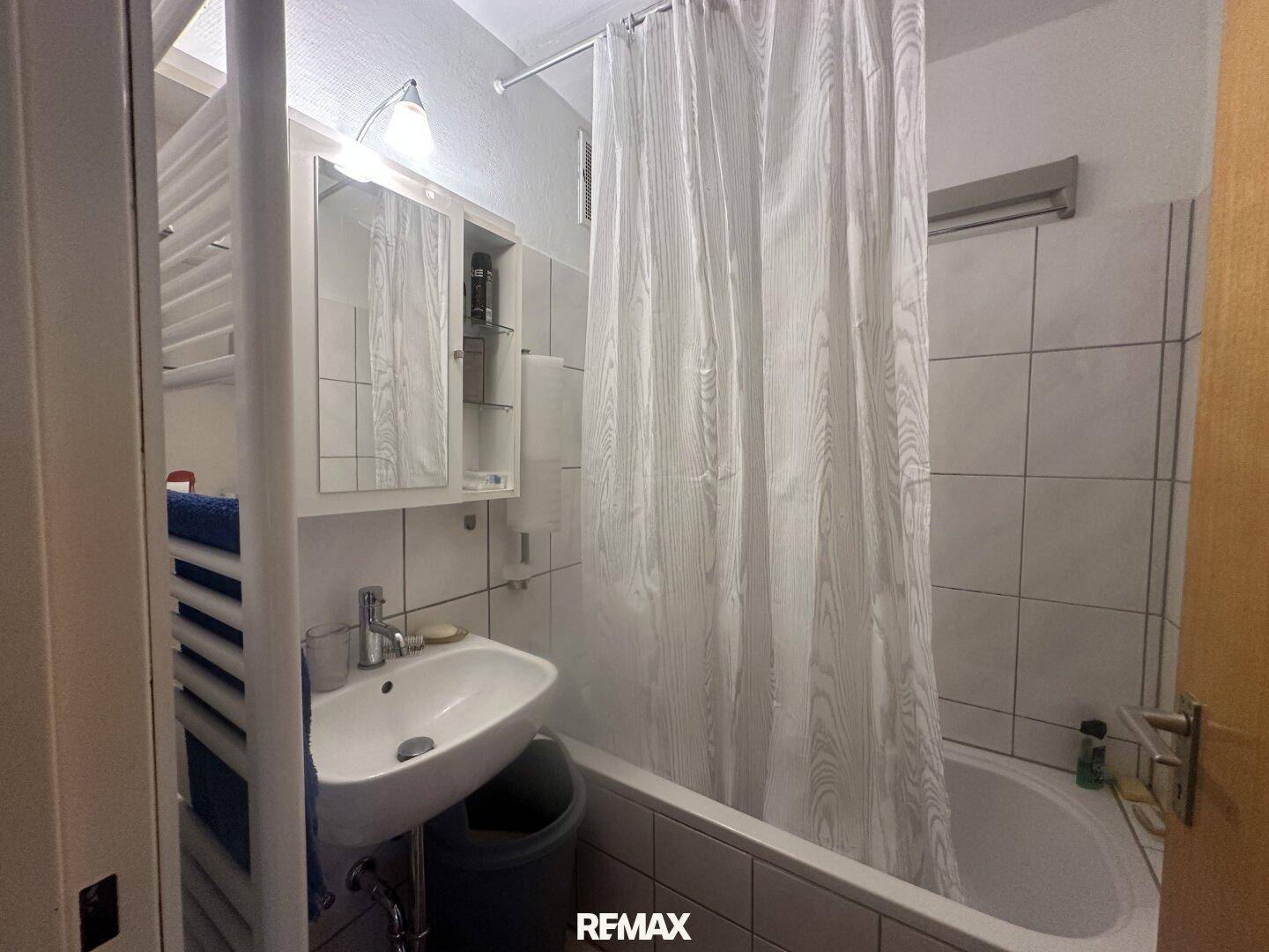 Funktionales Badezimmer mit Badewanne, Duschvorhang, Waschbecken und beheiztem Handtuchhalter.