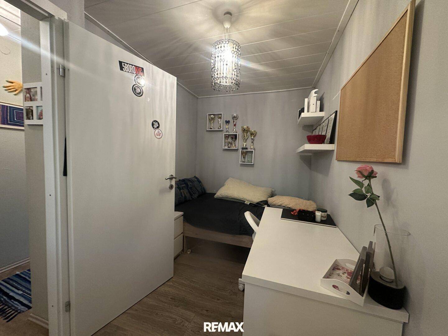 Kleines, helles Schlafzimmer mit Einzelbett, Schreibtisch und Laminatboden.