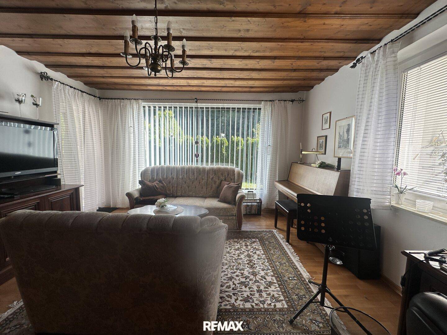 Wohnzimmer mit Holzbalkendecke, bequemen Sofas und einem Klavier am Fenster.