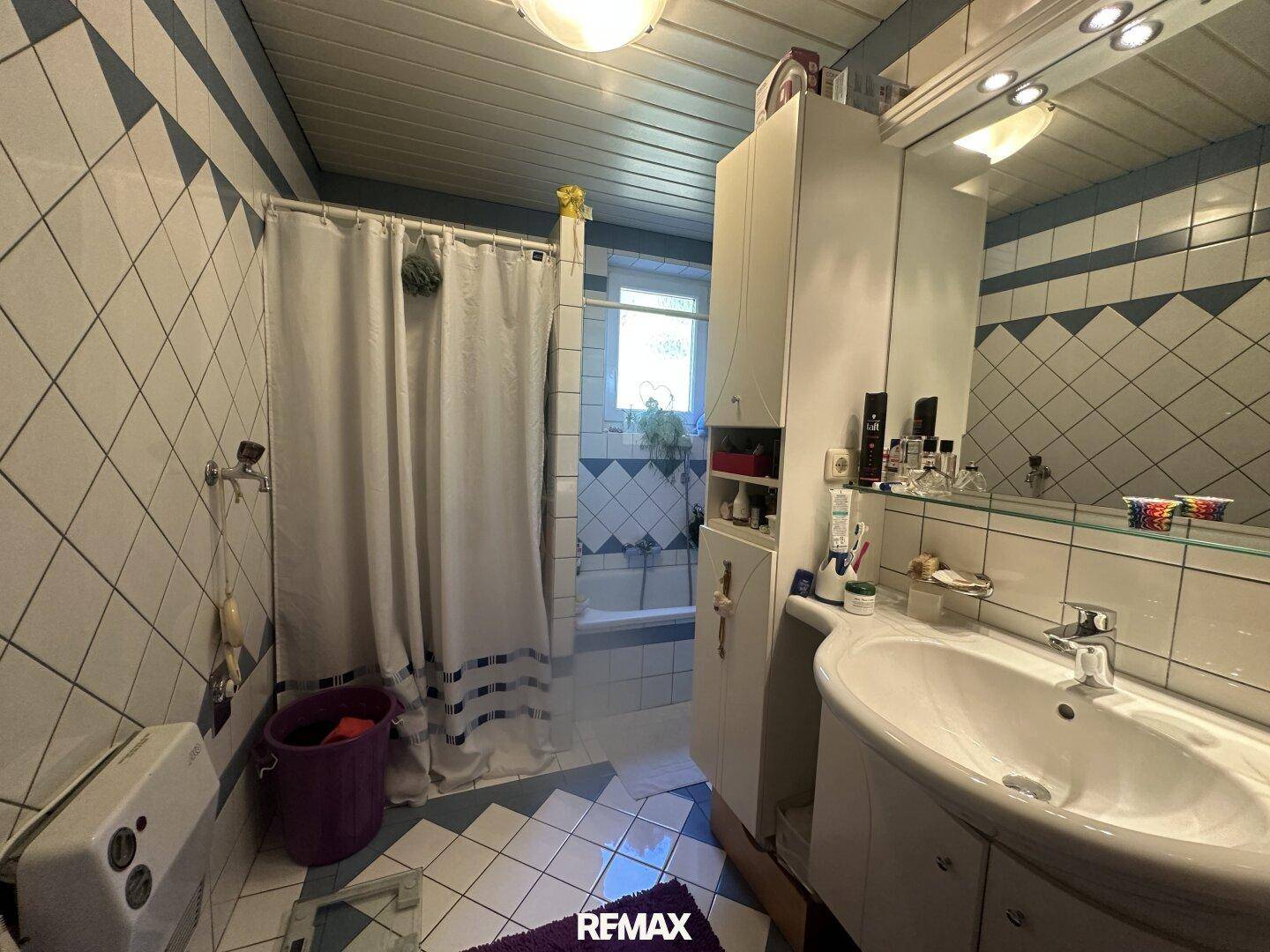 Badezimmer mit blau-weißen Fliesen, Waschbecken und Dusch-Badewannen-Kombination.