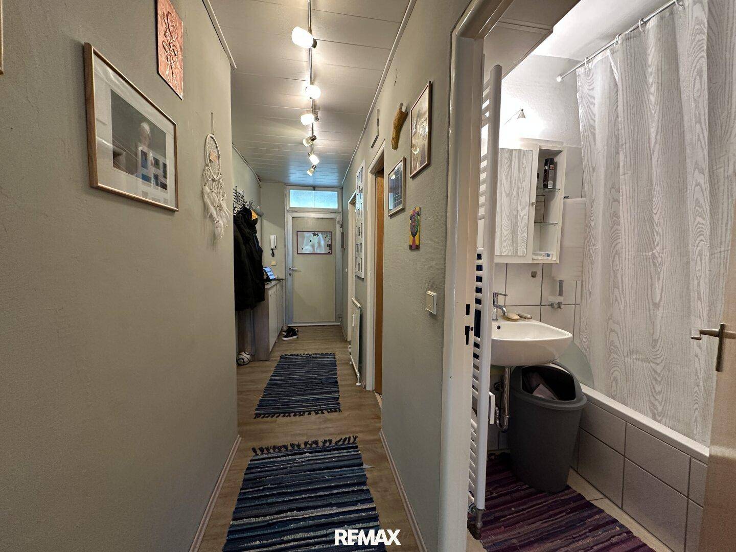 Langer Flur mit Holzfußboden, der zu einem Badezimmer mit Badewanne und Waschbecken führt.
