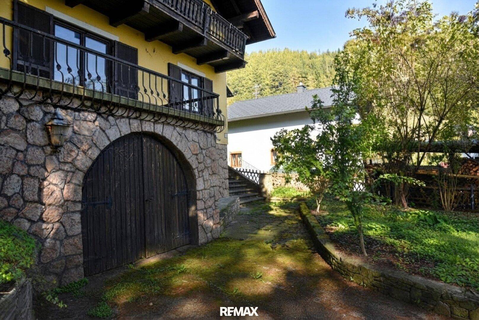 Steingemauerter Eingangsbereich mit Holztor und Treppe zum oberen Balkon.