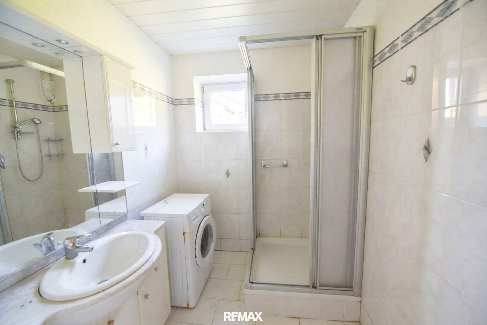 Badezimmer mit Dusche, Waschbecken, Waschmaschine und Fenster.