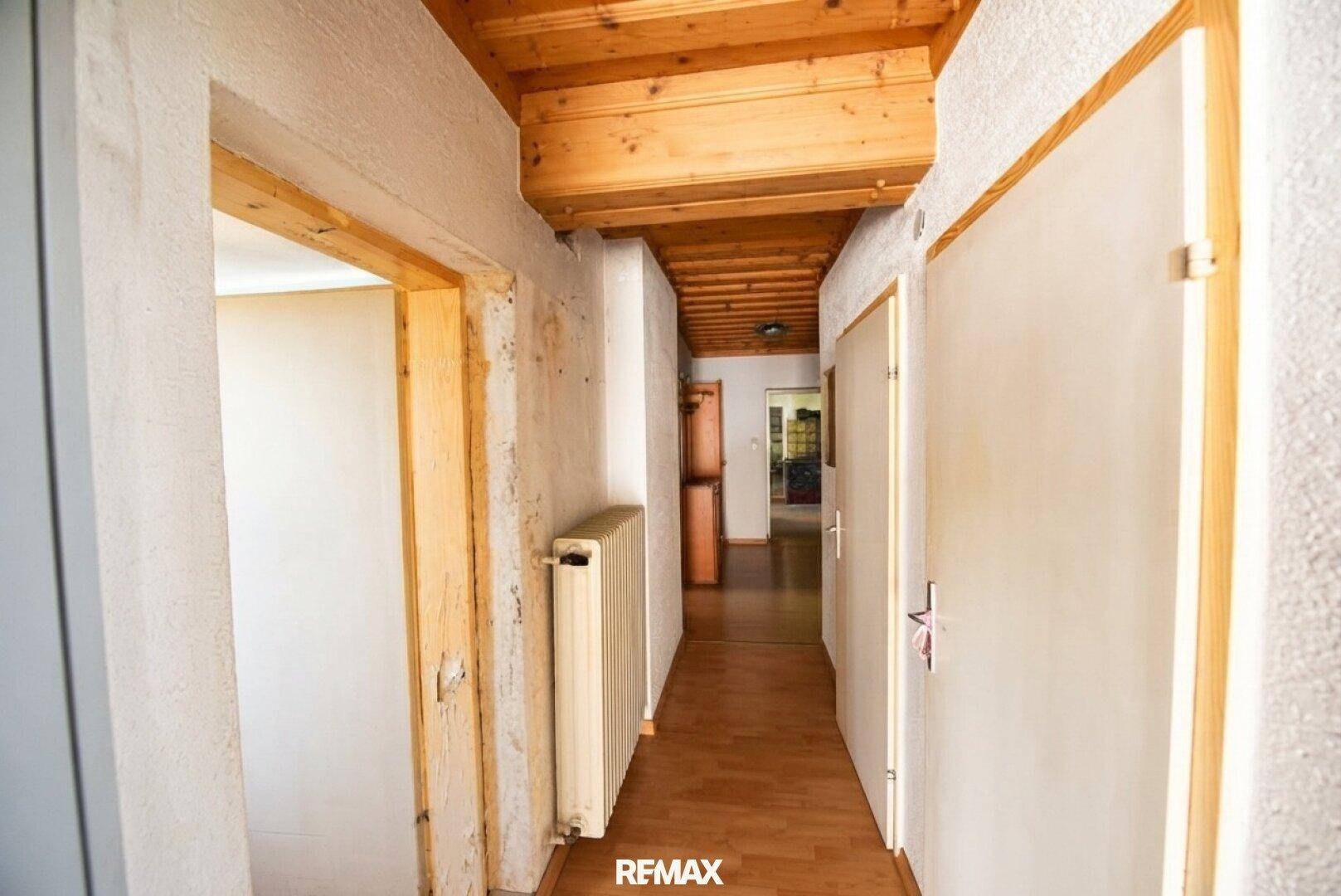 Schmaler Flur mit Holzbalkendecke, Heizkörper und Zugang zu weiteren Räumen.