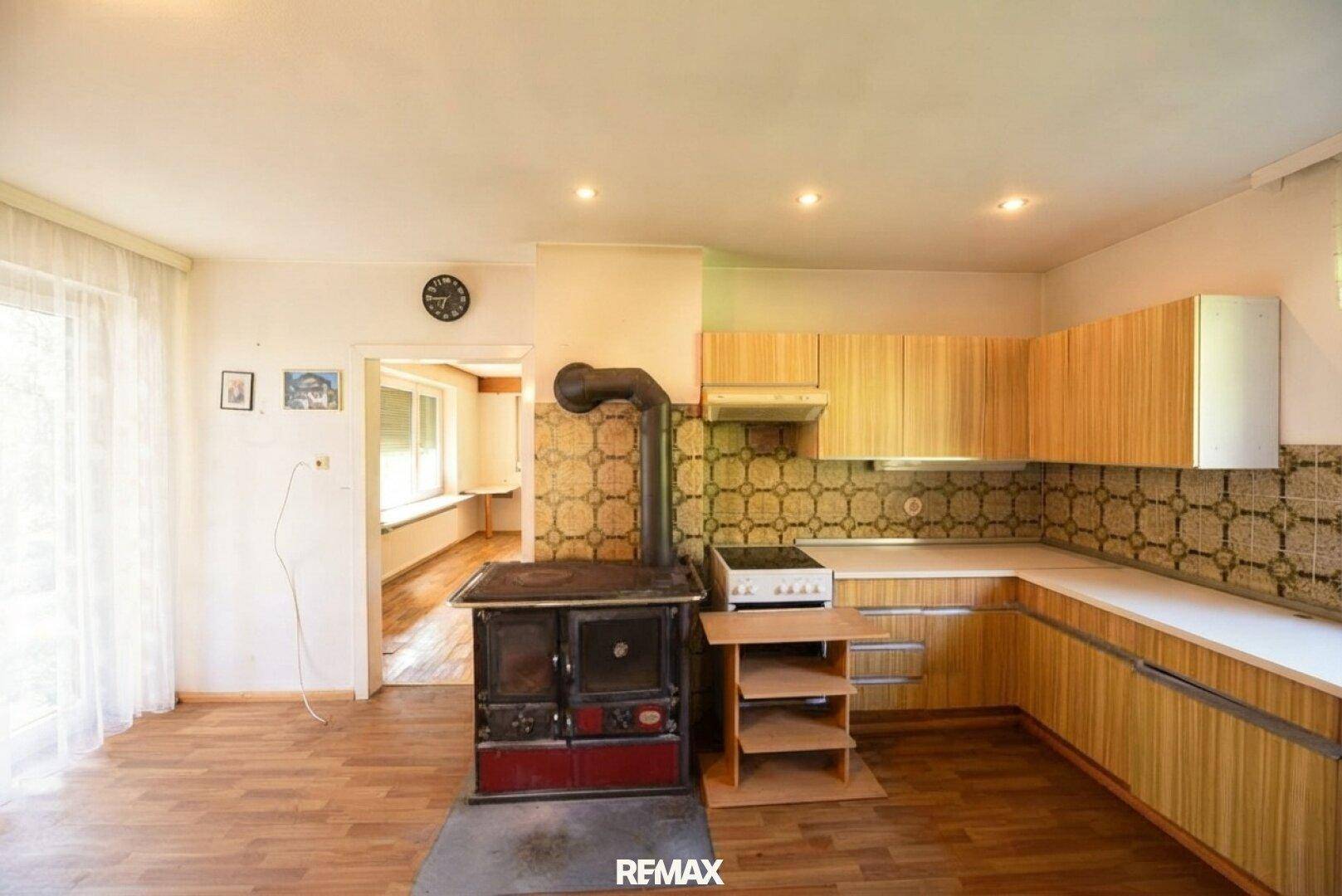 Helle Küche mit traditionellem Kachelofen, Holzschränken und Blick in den Nebenraum.