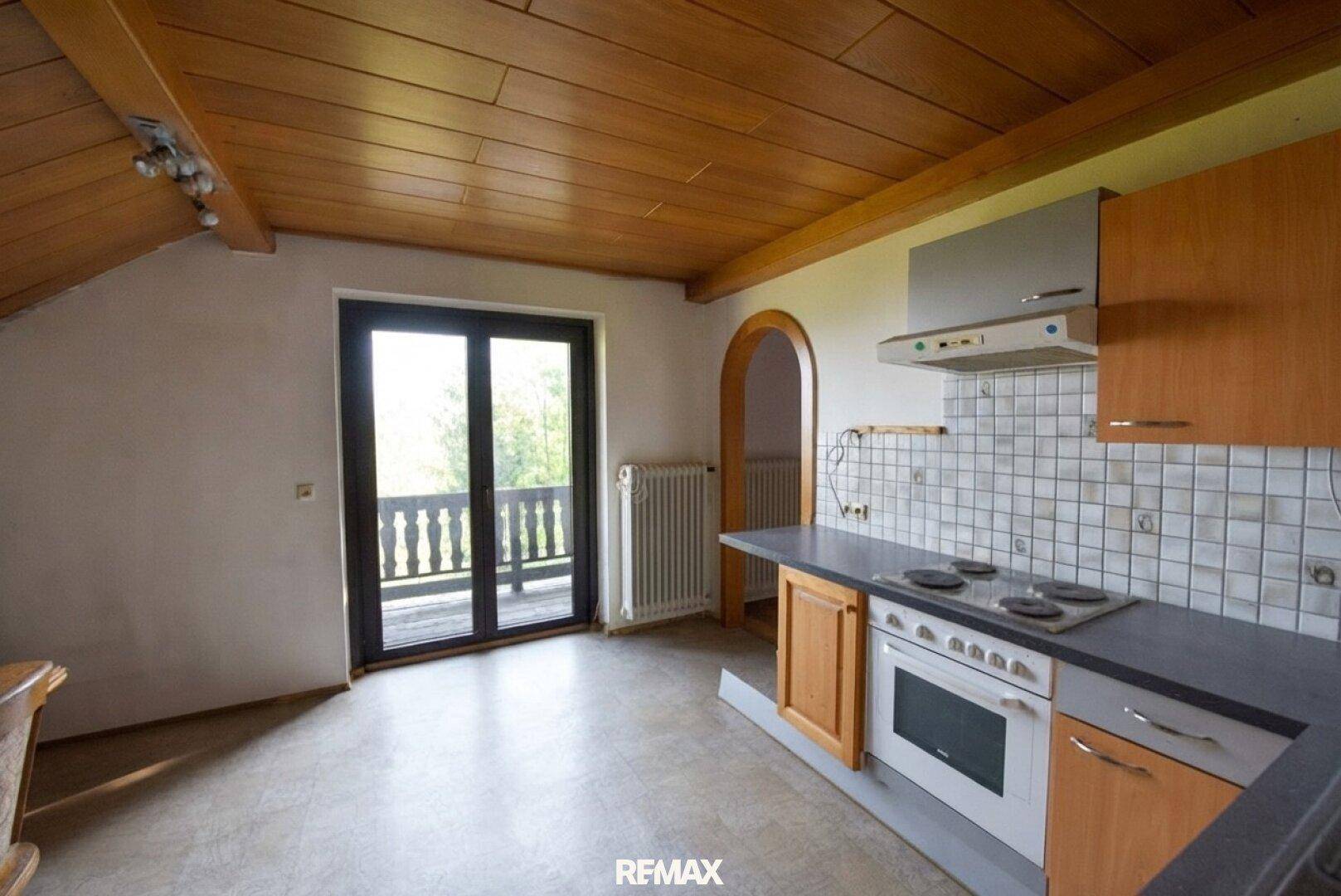 Dachgeschossküche mit Holzdecke, Einbauküche und Balkonzugang.