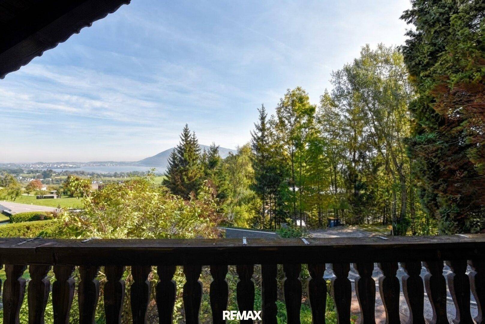 Balkon mit Holzgeländer und weitem Blick über die Landschaft und einen See.
