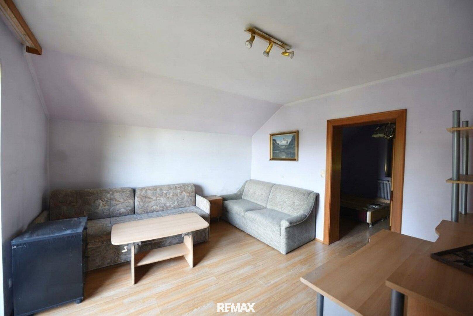 Gemütliches Dachgeschoss-Wohnzimmer mit Schrägen, Sofa und Holzboden.