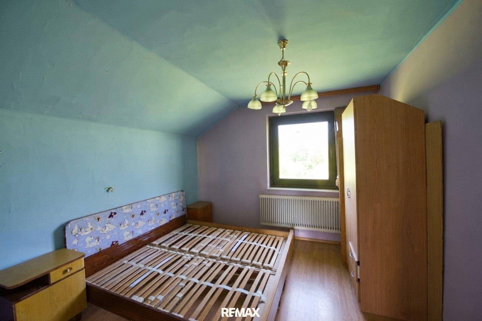 Dachgeschoss-Schlafzimmer mit Schrägen, Doppelbett und Fenster.